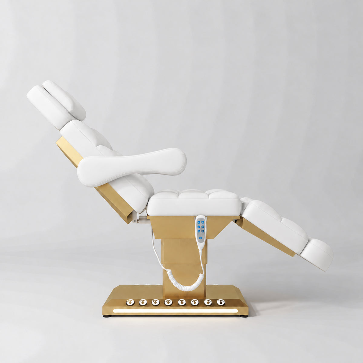 Manufakturo Orielle B White electric beauty bed shown from the side in a treatment position, with gold base and hand-held controller.