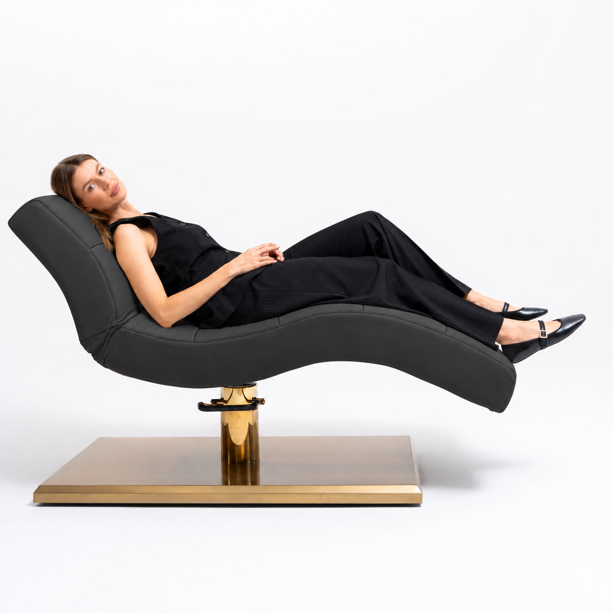 Manufakturo Prestige Black hydraulic beauty bed with a reclining client, showing contoured upholstery and gold base.