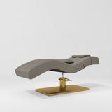 Manufakturo Prestige Deep Ash hydraulic eyelash bed, three-quarter side view with gold pedestal base and contoured upholstery.
