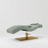 Manufakturo Prestige Olive hydraulic eyelash bed, three-quarter side view with gold pedestal base and contoured upholstery.