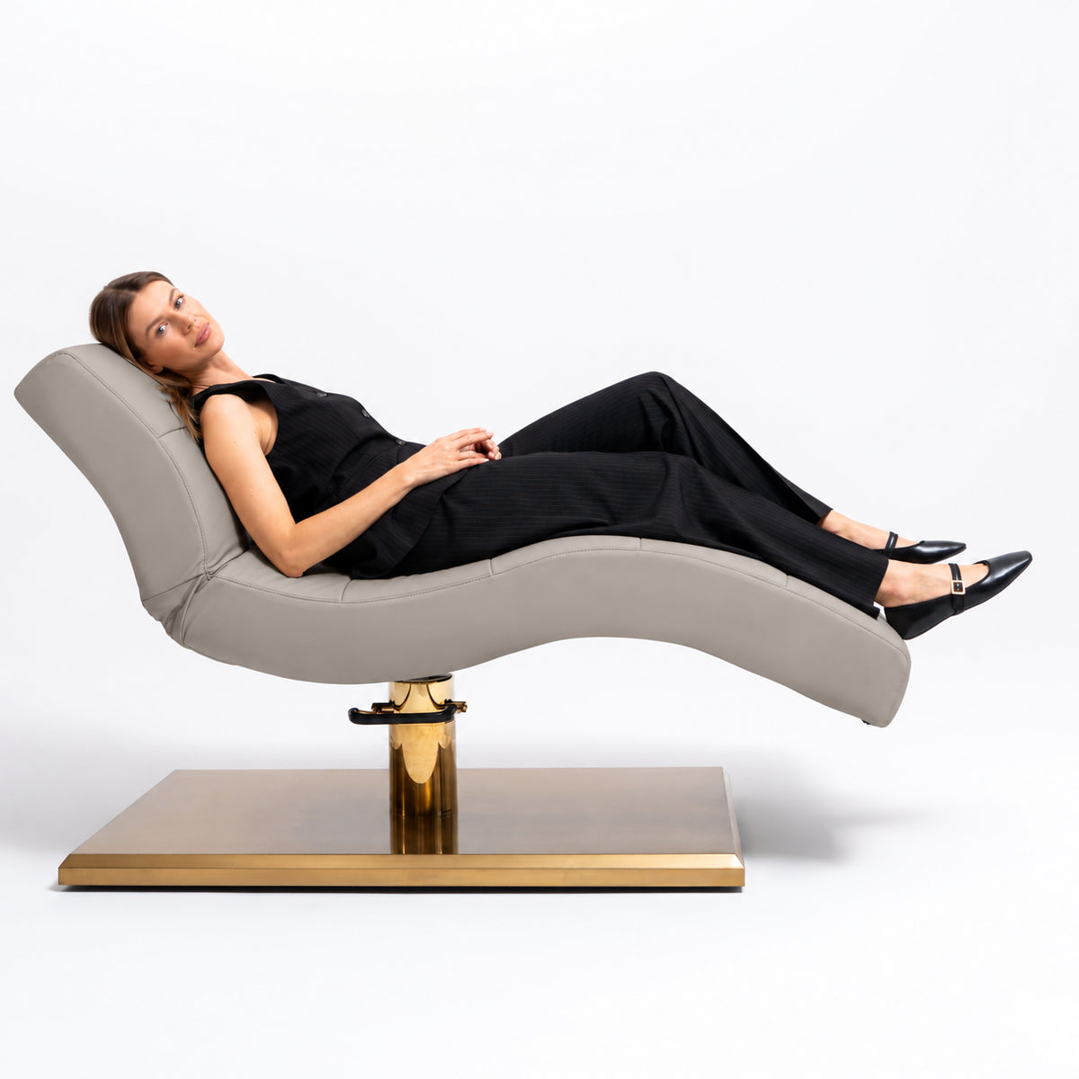 Manufakturo Prestige Pearl Greige hydraulic beauty bed with a reclining client, showing contoured upholstery and gold base.