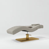 Manufakturo Prestige Pearl Greige hydraulic eyelash bed, three-quarter side view with gold pedestal base and contoured upholstery.