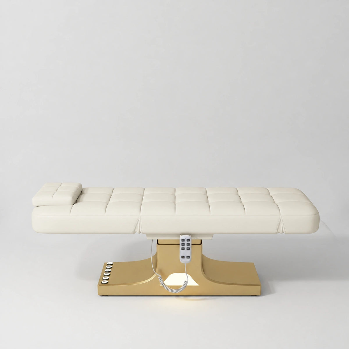 Manufakturo Saphir A Creamy electric beauty bed with gold base, flat lying position shown from the side, without armrests.