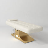 Manufakturo Saphir A Creamy electric beauty bed with gold base, flat lying position shown in a three-quarter view, without armrests.
