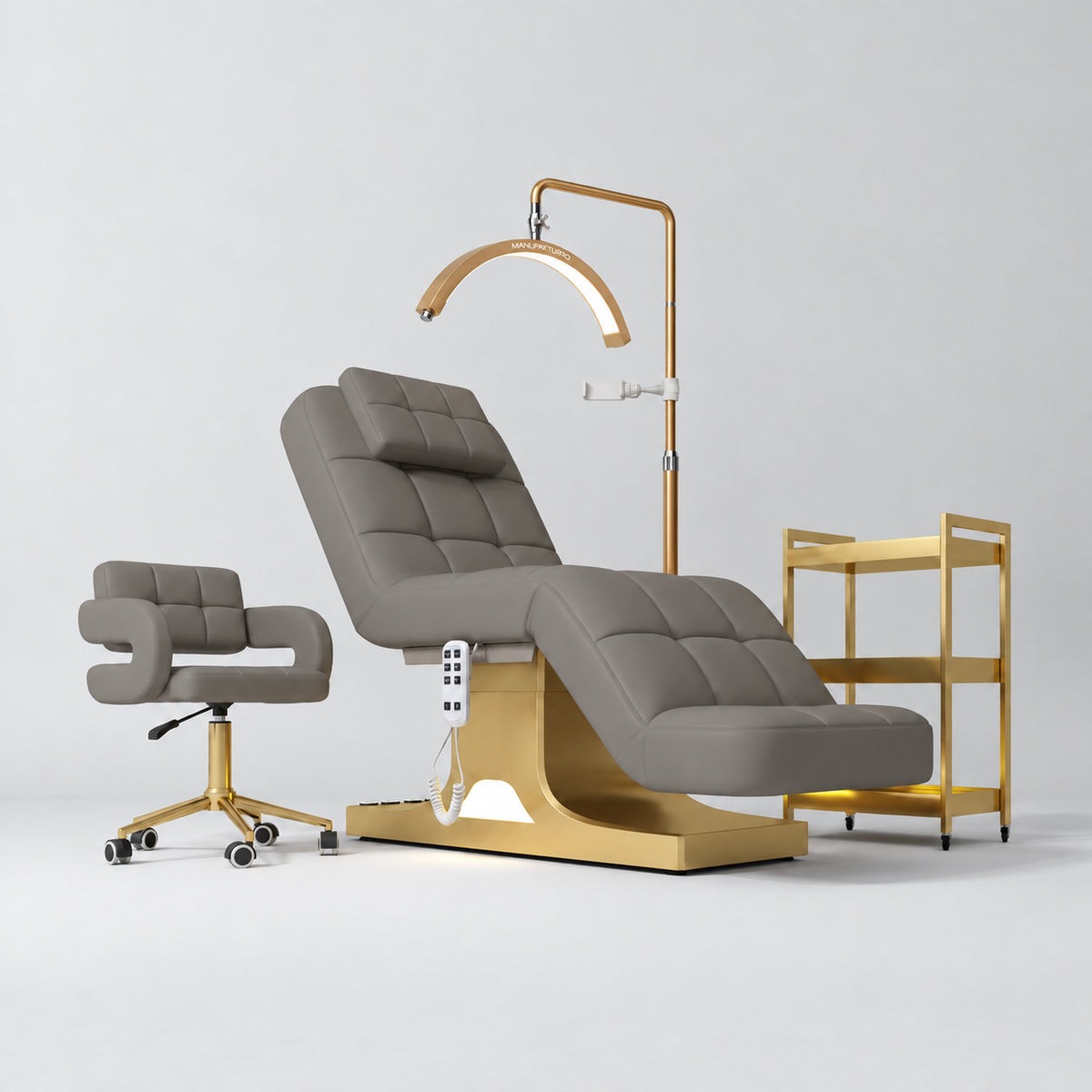 Manufakturo Saphir A Deep Ash four-piece beauty studio set with electric bed, Serenity salon chair, V3 Pro Gold lamp and empty three-tier gold trolley.