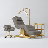 Manufakturo Saphir A Deep Ash four-piece beauty studio set with electric bed, Serenity salon chair, V3 Pro Gold lamp and empty three-tier gold trolley.