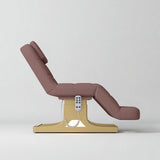 Manufakturo Saphir A Dusty Rose electric beauty bed with gold base, raised treatment position shown from the side, without armrests.
