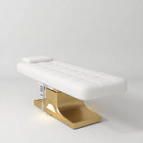 Manufakturo Saphir A White electric beauty bed with gold base, flat lying position shown in a three-quarter view, without armrests.
