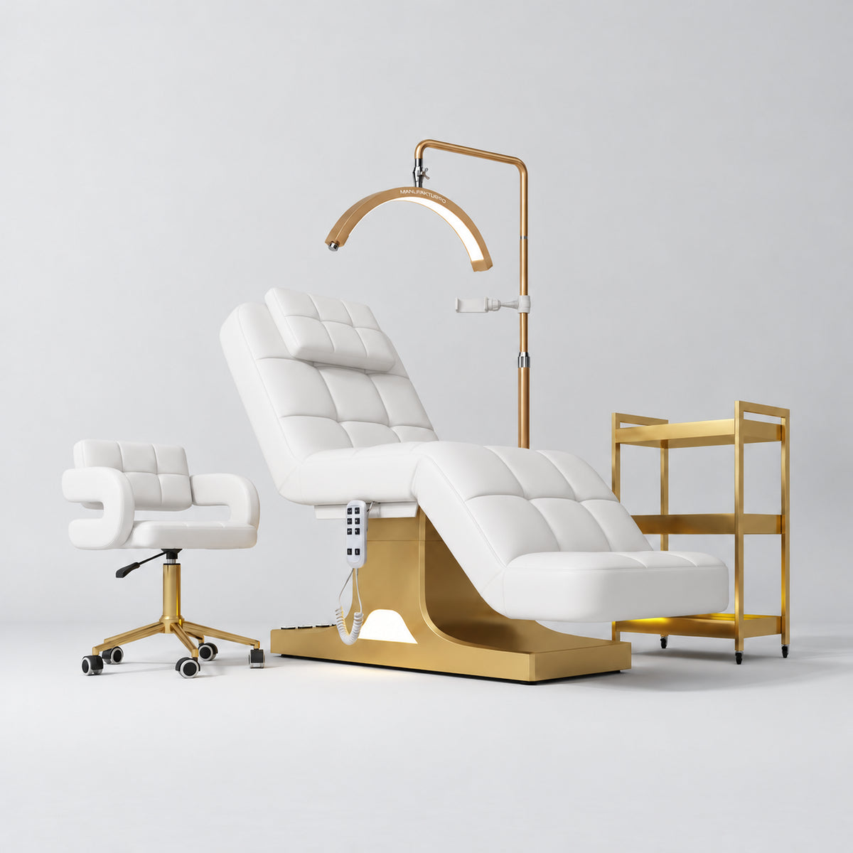 Manufakturo Saphir A White four-piece beauty studio set with electric bed, Serenity salon chair, V3 Pro Gold lamp and empty three-tier gold trolley.
