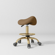 Manufakturo Selle Ergonomic Beauty Saddle Stool Caramel - Gold Base - displayed in a professional treatment-room setting