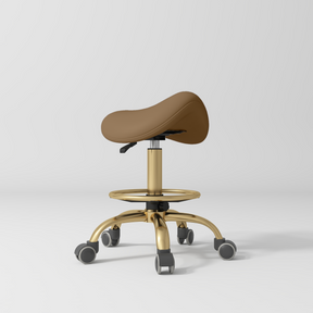 Manufakturo Selle Ergonomic Beauty Saddle Stool Caramel - Gold Base - displayed in a professional treatment-room setting