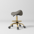 Manufakturo Selle Ergonomic Beauty Saddle Stool Deep Ash - Gold Base - displayed in a professional treatment-room setting