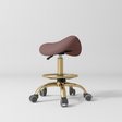 Manufakturo Selle Ergonomic Beauty Saddle Stool Dusty Rose - Gold Base - displayed in a professional treatment-room setting