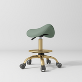 Manufakturo Selle Ergonomic Beauty Saddle Stool Olive - Gold Base - displayed in a professional treatment-room setting