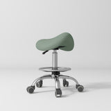 Manufakturo Selle Ergonomic Beauty Saddle Stool Olive - Silver Base - displayed in a professional treatment-room setting