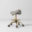 Manufakturo Selle Ergonomic Beauty Saddle Stool Pearl Greige - Gold Base - displayed in a professional treatment-room setting