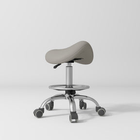 Manufakturo Selle Ergonomic Beauty Saddle Stool Pearl Greige - Silver Base - displayed in a professional treatment-room setting