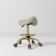 Manufakturo Selle Ergonomic Beauty Saddle Stool Stone Taupe - Gold Base - displayed in a professional treatment-room setting