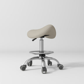 Manufakturo Selle Ergonomic Beauty Saddle Stool Stone Taupe - Silver Base - displayed in a professional treatment-room setting