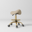 Manufakturo Selle Ergonomic Beauty Saddle Stool Warm Beige - Gold Base - displayed in a professional treatment-room setting