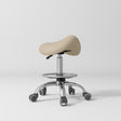 Manufakturo Selle Ergonomic Beauty Saddle Stool Warm Beige - Silver Base - displayed in a professional treatment-room setting