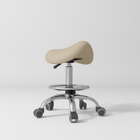 Manufakturo Selle Ergonomic Beauty Saddle Stool Warm Beige - Silver Base - displayed in a professional treatment-room setting