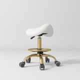 Manufakturo Selle Ergonomic Beauty Saddle Stool White - Gold Base - displayed in a professional treatment-room setting