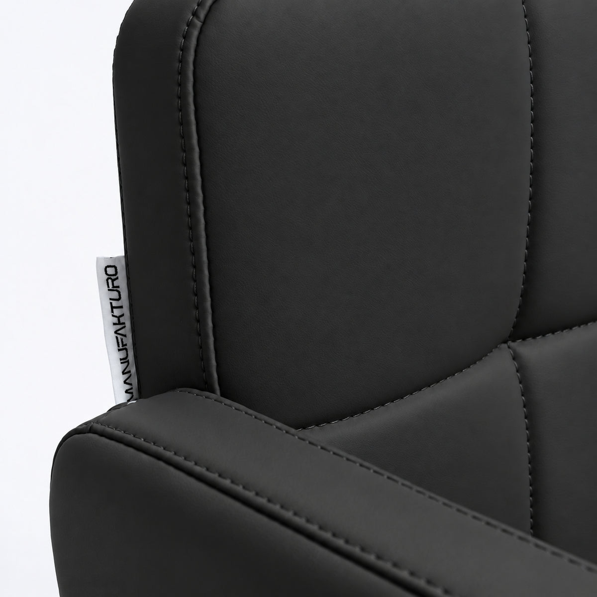 Close-up of Manufakturo Serenity Black salon chair upholstery, showing the stitched padded backrest, armrest piping and woven Manufakturo label.