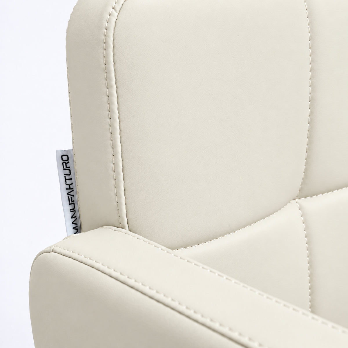 Close-up of Manufakturo Serenity Creamy salon chair upholstery, showing the stitched padded backrest, armrest piping and woven Manufakturo label.
