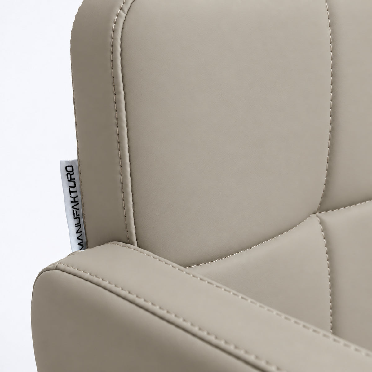 Close-up of Manufakturo Serenity Stone Taupe salon chair upholstery, showing the stitched padded backrest, armrest piping and woven Manufakturo label.