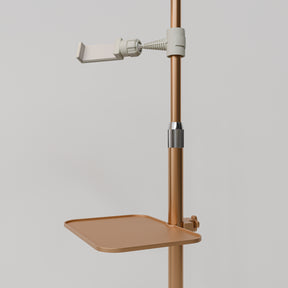 Close-up of the gold Manufakturo accessory tray clamped to a treatment lamp stand
