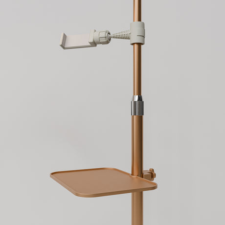 Close-up of the gold Manufakturo accessory tray clamped to a treatment lamp stand