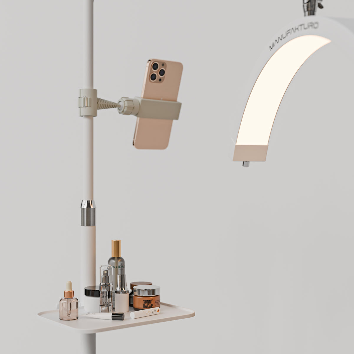White Manufakturo accessory tray holding bottles and jars beside a treatment lamp with a phone in its holder
