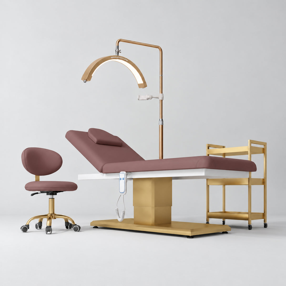 Manufakturo Chérie Dusty Rose four-piece salon set with treatment bed, matching salon chair, V3 Pro Gold lamp and empty gold three-tier beauty trolley.