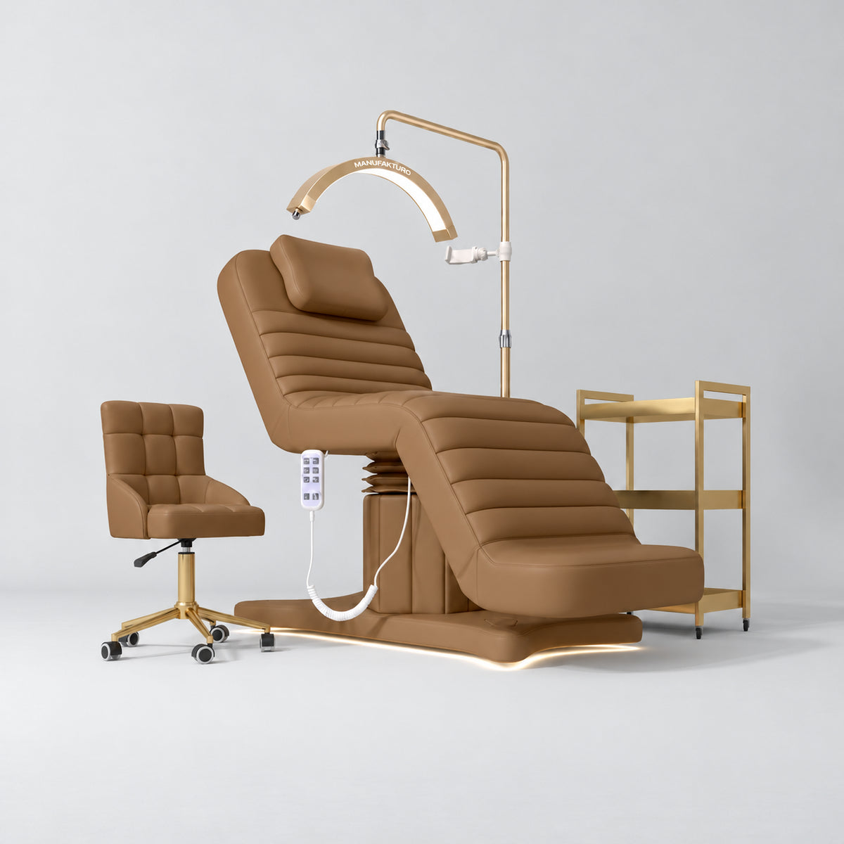 Manufakturo Grandeur Caramel four-piece salon set with treatment bed, matching salon chair, V3 Pro Gold lamp and empty gold three-tier beauty trolley.