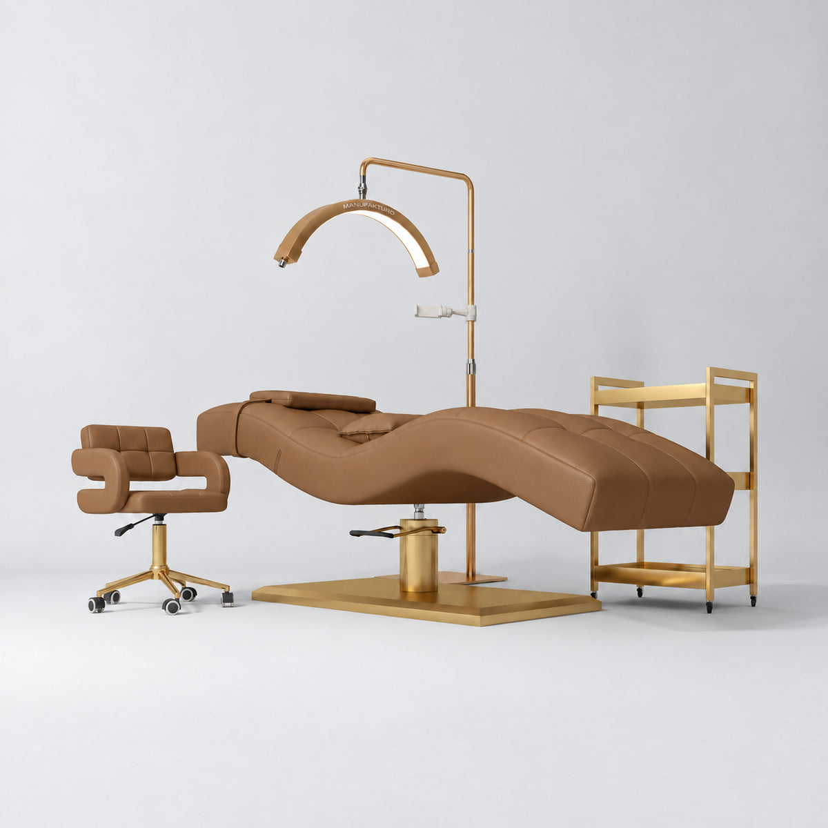 Manufakturo Prestige Caramel four-piece salon set with treatment bed, matching salon chair, V3 Pro Gold lamp and empty gold three-tier beauty trolley.