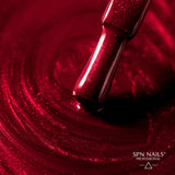 Brush dipped in SPN Nails UV/LED Gel Polish 1023 Kiss the Star, spreading vibrant red glitter polish on a glossy surface.