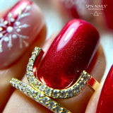 Close-up of red glitter nails with snowflake nail art, featuring SPN Nails UV/LED Gel Polish 1023 Kiss the Star and a gold ring.