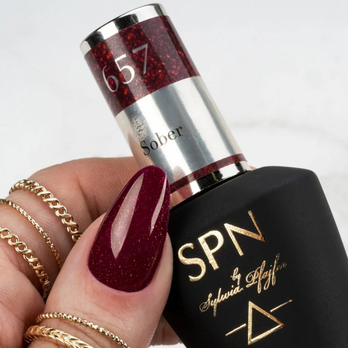 SPN Nails UV/LED Gel Polish 657 Sober bottle held by a hand with glittery red nails, highlighting its rich color and elegant design.